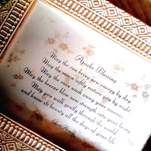 May include: A rectangular decorative frame with a textured, light-colored border containing a printed Apache Blessing. The text reads: May the sun bring new energy by day, May the moon softly restore you by night, May the rain wash away your worries, May the breeze blow new strength into your being, May you walk gently through the world and know its beauty all the days of your life. Elliott Arnold.