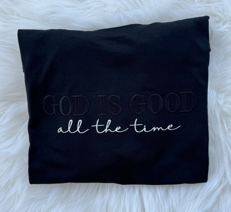 K&ouml;nnte beinhalten: Schwarzes T-Shirt mit dem gestickten Text "GOD IS GOOD all the time" in Wei&szlig;.