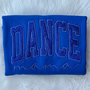 May include: A royal blue sweatshirt with the word "DANCE" in large, glittery, blue letters. The word "mama" is written in cursive below the word "DANCE".