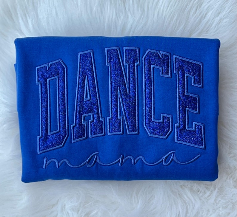 May include: A royal blue sweatshirt with the word "DANCE" in large, glittery, blue letters. The word "mama" is written in cursive below the word "DANCE".