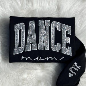 May include: Black sweatshirt with silver glitter lettering that reads "DANCE mom". The sleeve has white lettering that reads "Michaela, Gianna, Marisa" with a heart symbol.