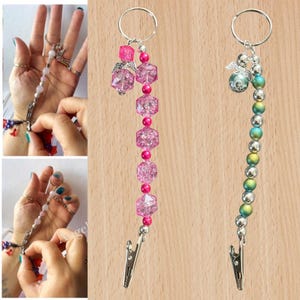 May include: Two beaded key ring lanyards with silver clips. One has pink faceted beads and a small angel charm. The other has iridescent beads and a silver angel charm. Both have silver key rings.