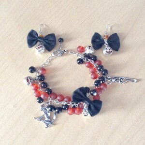May include: A Halloween-themed charm bracelet with red and black beads, a black bow, and various charms, including a pumpkin, a skeleton, and a witch. The bracelet also includes a pair of matching earrings with black bows and pumpkin charms.