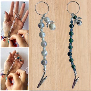 May include: Two beaded keychain lanyards with silver-tone clips. One features white and grey beads with angel charms, the other has green and blue beads with an angel charm. Both have a silver ring at the top.