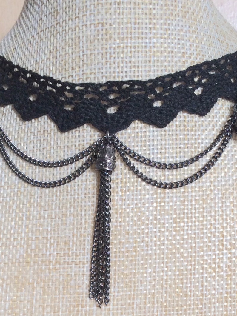 May include: Black lace choker necklace with a long chain tassel. The tassel is made of multiple chains and has a small crown-shaped charm at the top.