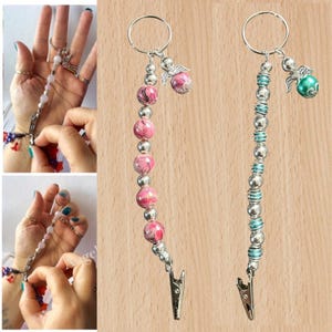 May include: Two beaded keychains with silver-tone clips. One has pink and silver beads, the other teal and silver. Each has a small angel charm and a keyring. Ideal for holding keys or small items.