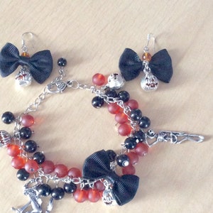 May include: A black and red beaded bracelet with charms, including a black bow, a skeleton, and a pumpkin. The bracelet also includes two matching earrings with black bows and pumpkin charms.