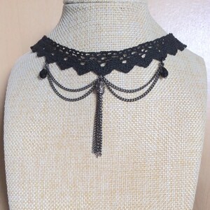 May include: Black crochet choker necklace with a dangling chain and tassel. The necklace has a delicate lace design and features a small metal charm.