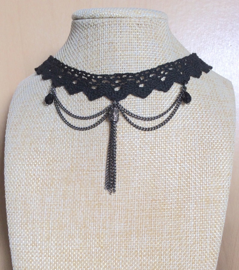 May include: Black crochet choker necklace with a dangling chain and tassel. The necklace has a delicate lace design and features a small metal charm.