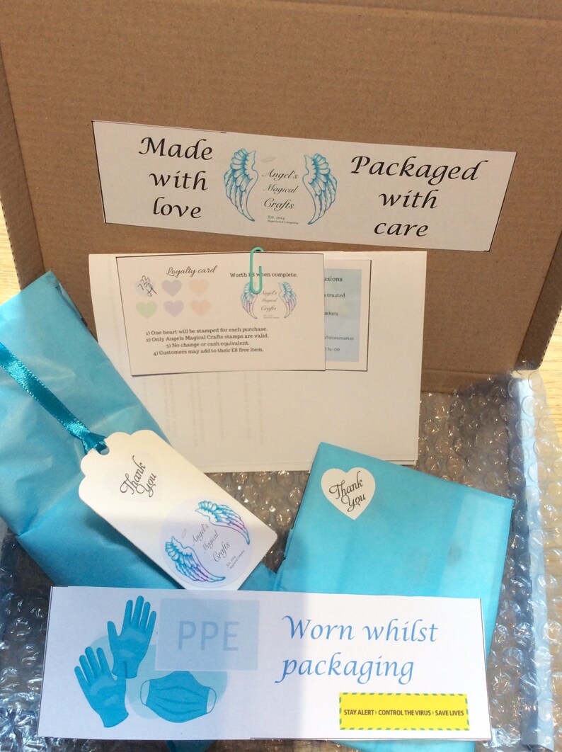 May include: A cardboard box with a blue and white tissue paper-wrapped package inside. The box is labeled "Made with love" and "Packaged with care." The tissue paper has a "Thank you" sticker with a heart on it. The box also has a sticker with a pair of blue gloves and a blue face mask, labeled "PPE Worn whilst packaging." The sticker also has the text "Stay alert - Control the virus - Save lives."