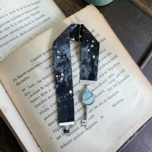 May include: Black velvet bookmark with gold star detailing and a silver key pendant. The bookmark is shown on an open book with aged pages and handwritten text.