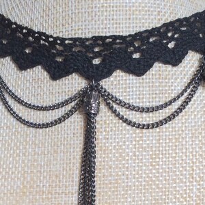 May include: Black lace choker necklace with a long chain tassel. The tassel is made of multiple chains and has a small crown-shaped charm at the top.