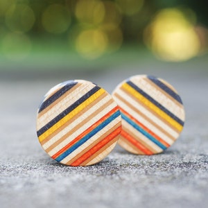 Peut inclure: Deux boucles d'oreilles rondes en bois avec un motif rayé dans des tons de bleu, jaune, orange et noir.