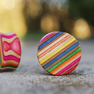 May include: Two colourful wooden ear gauges, one with a rainbow striped pattern and the other with a pink and rainbow pattern.