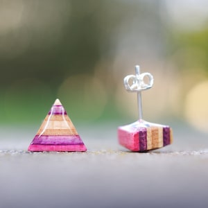 Puede incluir: Un par de pendientes en forma de triángulo hechos de madera con rayas rosas, moradas y marrones. Los pendientes tienen postes de plata.