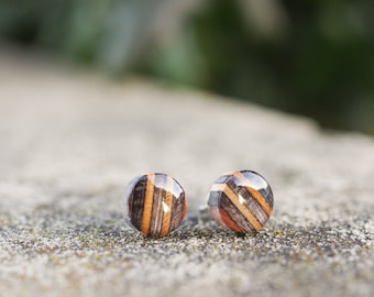 May include: A pair of round wooden earrings with a striped pattern in shades of brown, black, and beige.