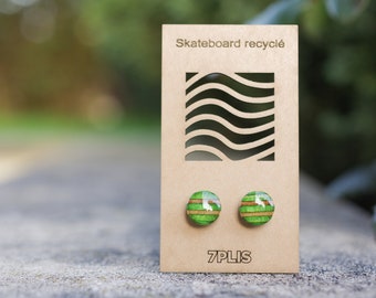 May include: Round stud earrings with a green and brown striped design, displayed on a cardboard backing. The earrings are made from recycled skateboard material. The text "Skateboard recyclé" and "7PLIS" are visible.