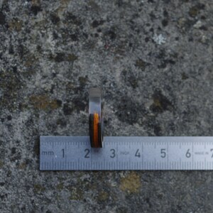 May include: A wooden ring with black and orange stripes, measured against a ruler. The ring is approximately 2 centimetres wide.