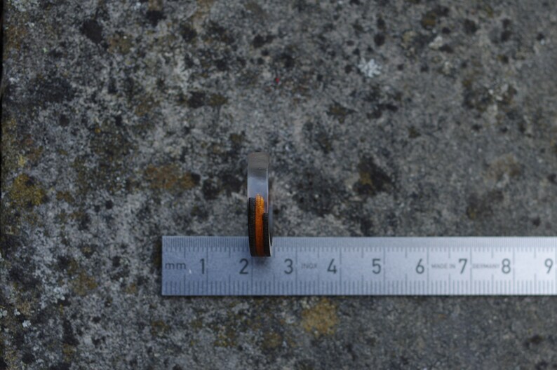 May include: A wooden ring with black and orange stripes, measured against a ruler. The ring is approximately 2 centimetres wide.