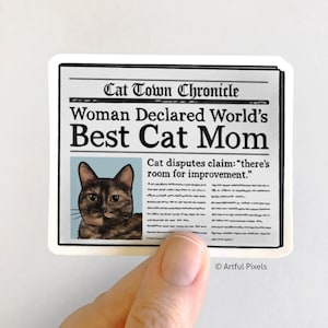Puede incluir: Un titular de peri&oacute;dico humor&iacute;stico que anuncia a una mujer como la "Mejor Mam&aacute; Gato del Mundo." Un gato atigrado aparece en el art&iacute;culo, con la leyenda "El gato disputa la afirmaci&oacute;n: "hay margen de mejora."