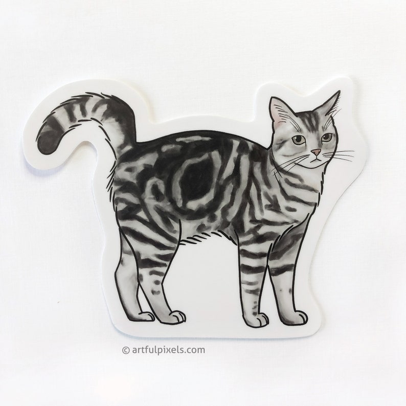 Pode incluir: Um adesivo ilustrado em preto e branco de um gato tigrado em p&eacute; sobre suas quatro patas. O gato est&aacute; olhando para a direita da imagem. O adesivo tem um fundo branco e o texto "artfulpixels.com" &eacute; impresso na parte inferior central do adesivo.