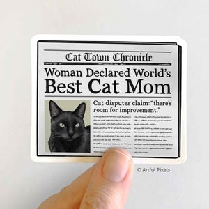 May include: A black and white newspaper clipping with the headline "Woman Declared World's Best Cat Mom". A black cat with green eyes is pictured in the article. The text below the headline reads "Cat disputes claim: "there's room for improvement.""