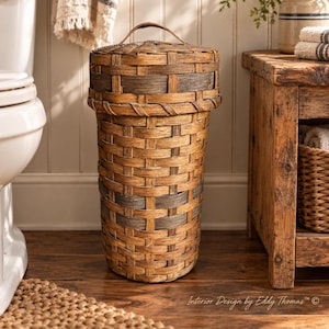 May include: A tall, cylindrical woven basket with a matching lid and a small handle on top. The basket features a pattern of light brown and dark grey woven strips in a vertical and horizontal weave, creating a textured, multi-toned appearance.
