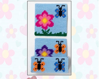 Puede incluir: Un juego de tres posavasos de lona plástica con un diseño de flores y mariposas. Los posavasos son azules con un borde blanco y presentan una flor rosa con un centro amarillo, una flor morada con un centro amarillo y dos mariposas, una naranja y otra azul.