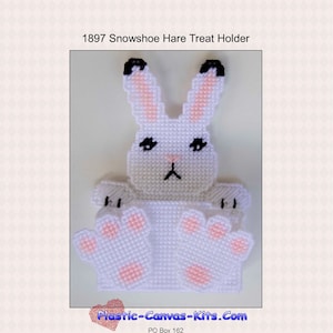 May include: White plastic canvas pattern of a snowshoe hare with pink ears and paws. The pattern is for a treat holder and includes the text "1897 Snowshoe Hare Treat Holder" and "Plastic-Canvas-Kits.com".