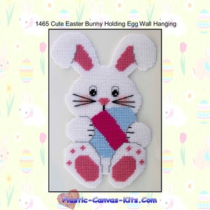 May include: White plastic canvas pattern of a cute Easter bunny holding a blue and pink egg. The bunny has pink ears, pink paws, and black whiskers. The pattern is titled "1465 Cute Easter Bunny Holding Egg Wall Hanging".