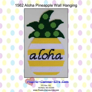 Può includere: Un'appendice da parete a forma di ananas in tela plastica gialla e bianca con la parola "aloha" in lettere nere. L'ananas ha una cima verde con pois verdi.