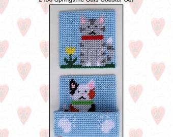 Puede incluir: Un conjunto de dos patrones de posavasos de lona plástica con motivos de gatos. El primer posavasos presenta un gato gris con un collar rojo sentado frente a una flor amarilla. El segundo posavasos presenta un gato calico con un collar verde y huellas de patas. El patrón se titula "2190 Springtime Cats Coaster Set".