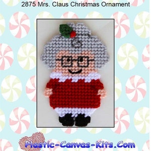 May include: A plastic canvas pattern for a Christmas ornament featuring Mrs. Claus. The pattern shows a cartoon-style Mrs. Claus with a red dress, white collar, and black shoes. She is wearing glasses and has gray hair. The pattern is on a blue background with white and pink candy cane designs.