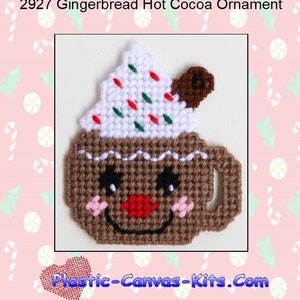 May include: A brown gingerbread hot cocoa ornament with a white whipped cream topping, red and green sprinkles, and a brown chocolate stick. The ornament has a smiling face with pink cheeks and a red nose.