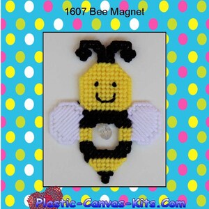 May include: A yellow and black bee magnet with white wings. The bee has a smiling face and a black stripe around its middle. The bee is on a white plastic canvas. The text "1607 Bee Magnet" is at the top of the image.