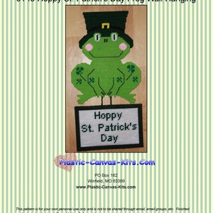 Pode incluir: Um sapo verde usando um chapéu verde com uma fivela dourada, segurando um sinal que diz "Hoppy St. Patrick's Day". O sapo está sentado em um fundo branco com listras verdes.