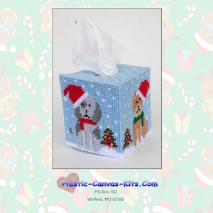 May include: A blue and white plastic canvas tissue box cover with a Christmas theme. The cover features two dogs wearing Santa hats and a Christmas tree. The text "Plastic-Canvas-Kits.com" is printed on the cover.