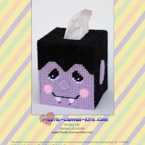 Op de afbeelding: Een handgemaakte vampier tissuebox cover. De zwarte en paarse cover heeft een vampier gezicht met roze wangen, zwarte ogen en twee tanden. De tissuebox is vierkant en heeft een tissue die uit de bovenkant steekt. De tekst "0793 Vampire Tissue Topper" staat bovenaan.