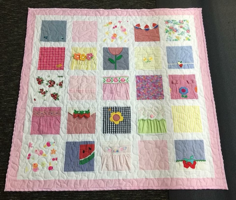 May include: A square patchwork quilt featuring a pink border and a white background with quilted patterns. The quilt consists of twenty-five individual squares, each displaying various fabric textures, floral prints, gingham patterns, and appliqu&eacute;d motifs.