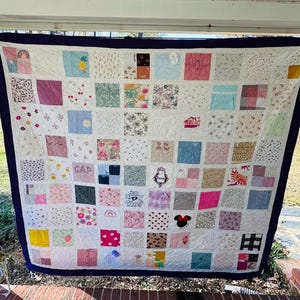 May include: A memory quilt composed of numerous square fabric patches featuring various patterns, colors, and embroidered designs, including a Minnie Mouse icon, a crown, and the text GAP, all framed by a solid dark blue border with white stitching.