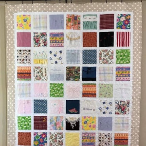 May include: A memory quilt featuring a grid of forty-nine square fabric patches with diverse patterns, including floral, plaid, and striped designs, surrounded by a beige border with white polka dots. One patch displays the embroidered name AlexGrace.