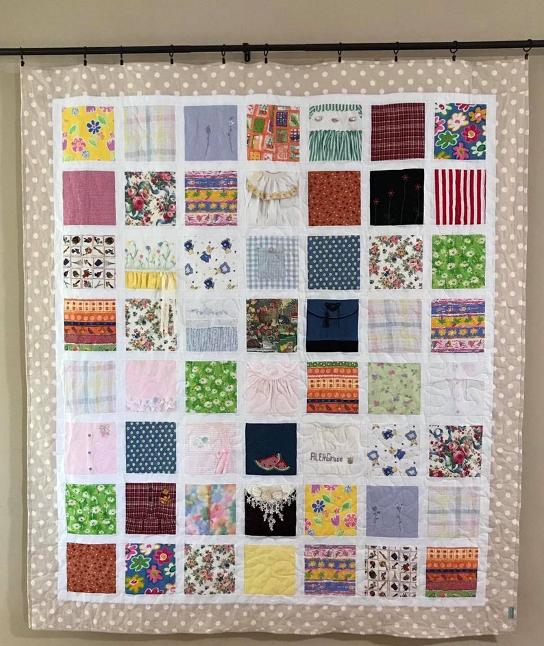 May include: A memory quilt featuring a grid of forty-nine square fabric patches with diverse patterns, including floral, plaid, and striped designs, surrounded by a beige border with white polka dots. One patch displays the embroidered name AlexGrace.