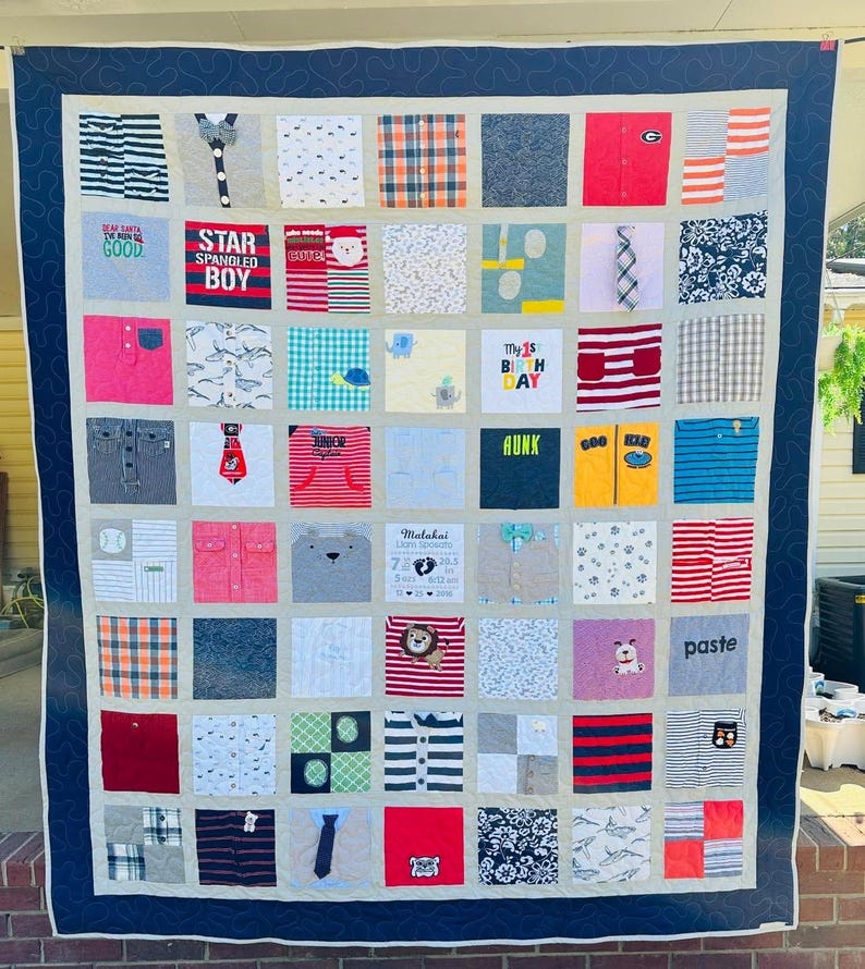 May include: A memory quilt composed of numerous square fabric patches featuring various patterns, colors, and graphic prints from children's clothing. The quilt has a dark blue border with a swirling stitch pattern and a light gray inner border.