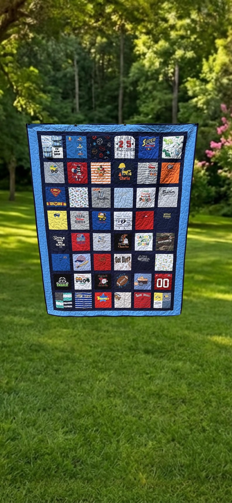 May include: A memory quilt constructed from various square fabric patches featuring diverse graphic prints, embroidered text, and sports themes. The quilt has a dark blue border and a light blue inner frame, with a grid layout of colorful squares.