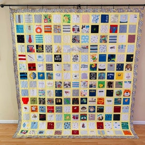 May include: A large memory quilt composed of numerous square fabric patches featuring various graphic prints, patterns, and text including "All American Boy," "Little Brother," and "Los Angeles." The quilt has a yellow grid and a gray border.