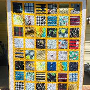 May include: A patchwork quilt featuring a grid of square fabric panels with various patterns, including stripes, plaids, and graphic prints. The squares are separated by mustard yellow sashing and framed by a white border with a swirling pattern.