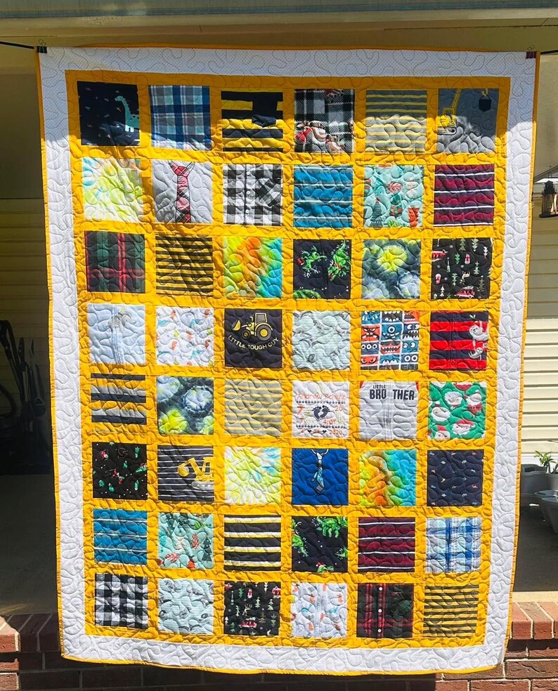 May include: A patchwork quilt featuring a grid of square fabric panels with various patterns, including stripes, plaids, and graphic prints. The squares are separated by mustard yellow sashing and framed by a white border with a swirling pattern.