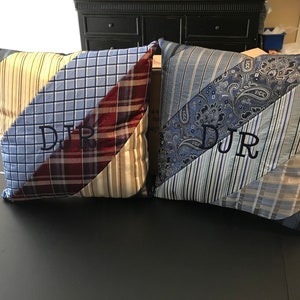 May include: Two decorative throw pillows with a patchwork design made from various patterned fabrics, including stripes, plaid, and paisley. Each pillow features embroidered initials "DJR" in a dark thread. The pillows are on a black surface.