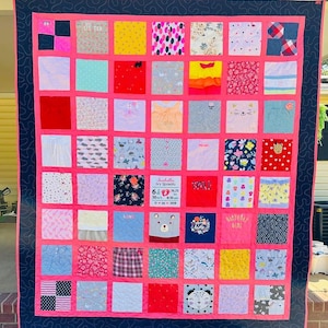 May include: A memory quilt composed of numerous square fabric patches featuring various patterns, colors, and graphics. A central white patch displays the text Isabella Ivy Sposato, 6 lbs 10 oz, 19.75 in, 8:10 am, 11-30-2018. The quilt has a bright pink border and a dark navy blue outer frame with a swirling stitched pattern.