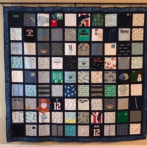 May include: A large square memory quilt composed of numerous fabric squares featuring various patterns, colors, and graphics, including text like "Big Brother," "Happy," and "Brady 12." The quilt is framed by a dark blue border and hangs from a black rod.